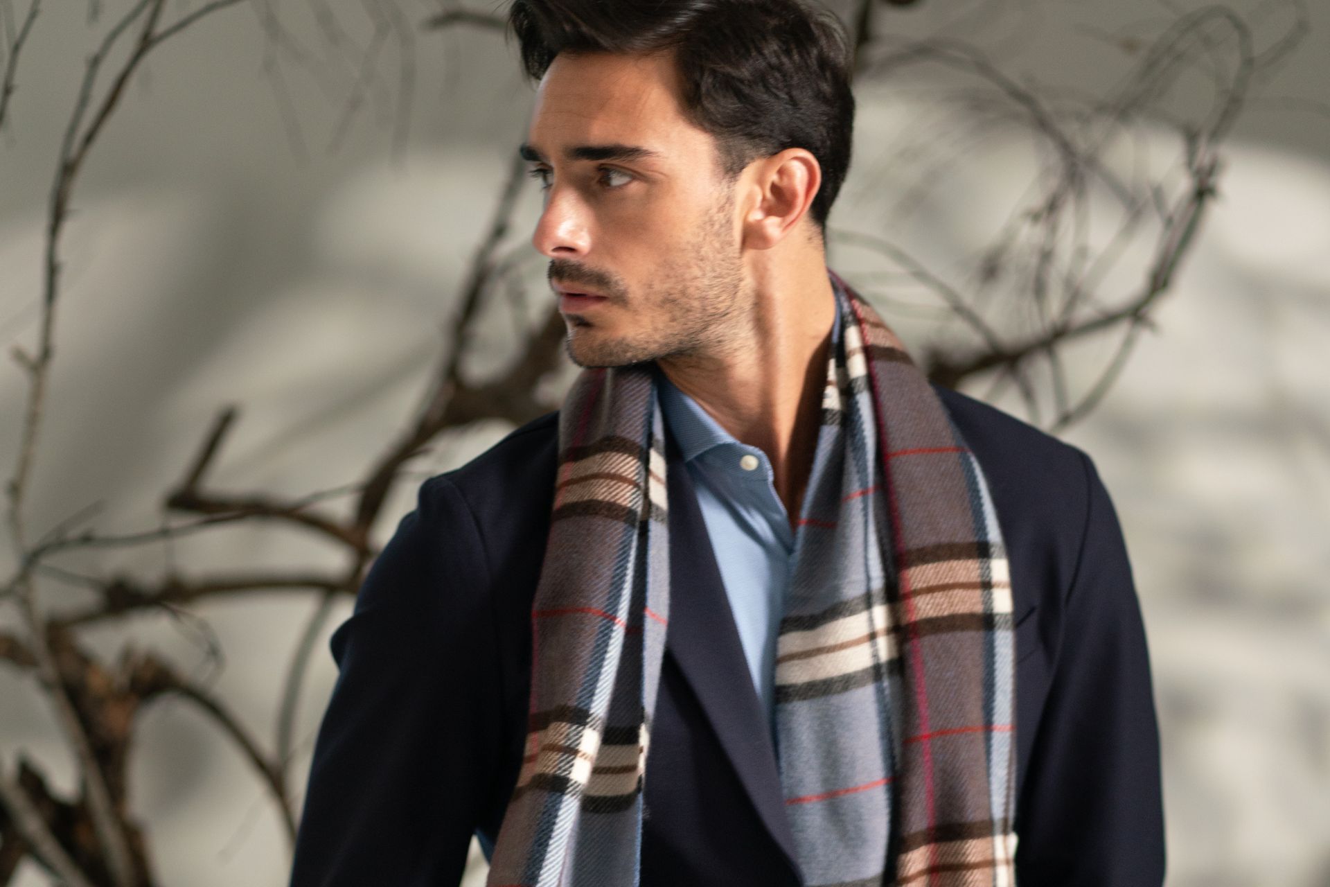 Uomo con giacca blu in tessuto tecnico, camicia azzurra e sciarpa madras