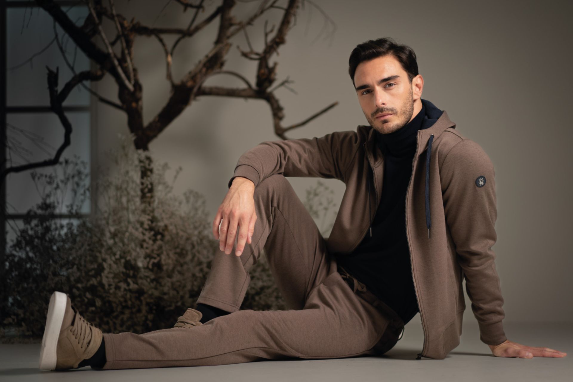 Uomo seduto che indossa felpa e pantaloni sportivi color tortora e dolcevita blu