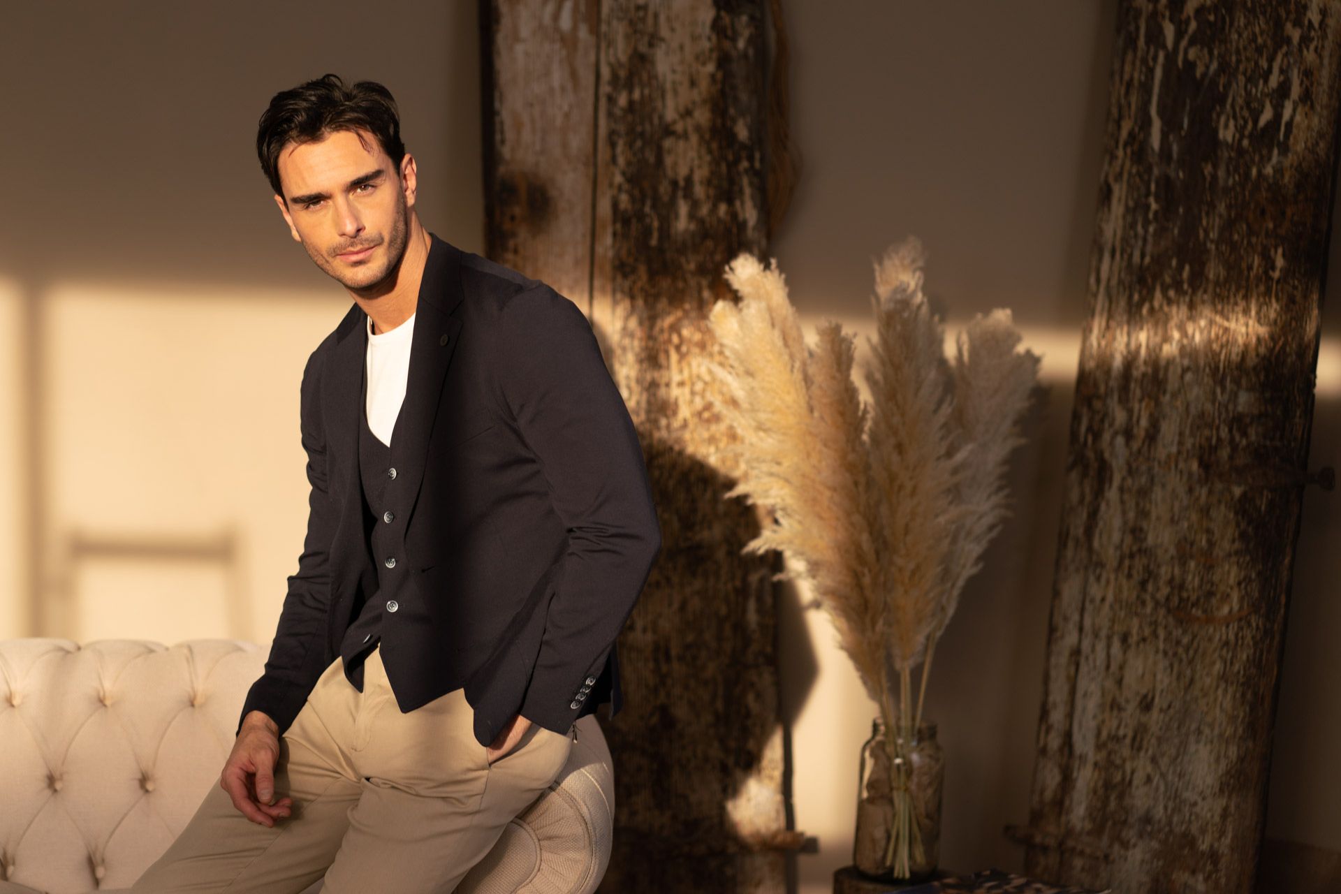 Uomo seduto sul divano mentre indossa giacca con gilet, t-shirt e pantaloni chinos per un outfit elegante casual